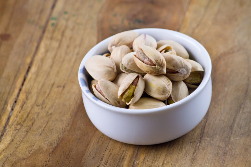 pistachios in a white bowl on a wood grain background